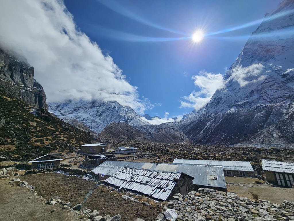 Karla kaplı dağların ve bulutlu bir gökyüzünün arasında yer alan dağ evleri ile doğal bir manzara.