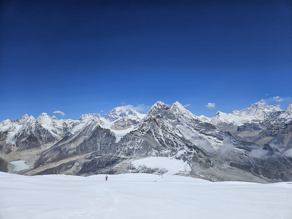 Buzullarla kaplı dağlar arasında kaybolmuş bir trekerin görüntüsü, net bir mavi gökyüzü altında trekking yolu boyunca ilerliyor.
