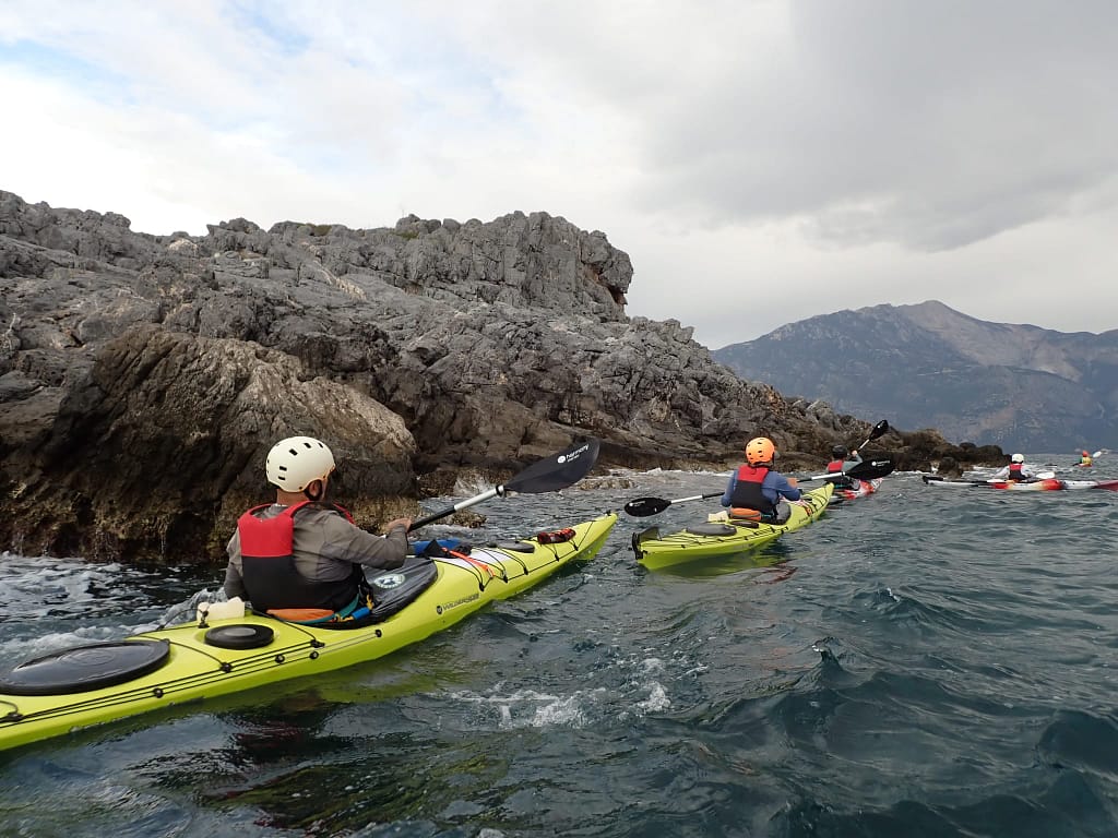 Deniz kayığına binen kişiler, kayalıklara yakın sularda kürek çekiyor.