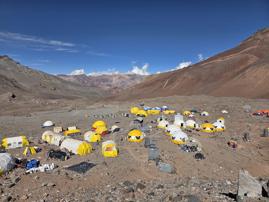 Dağlık bir alanda yer alan çeşitli renkli çadırların bulunduğu bir kamp alanı.