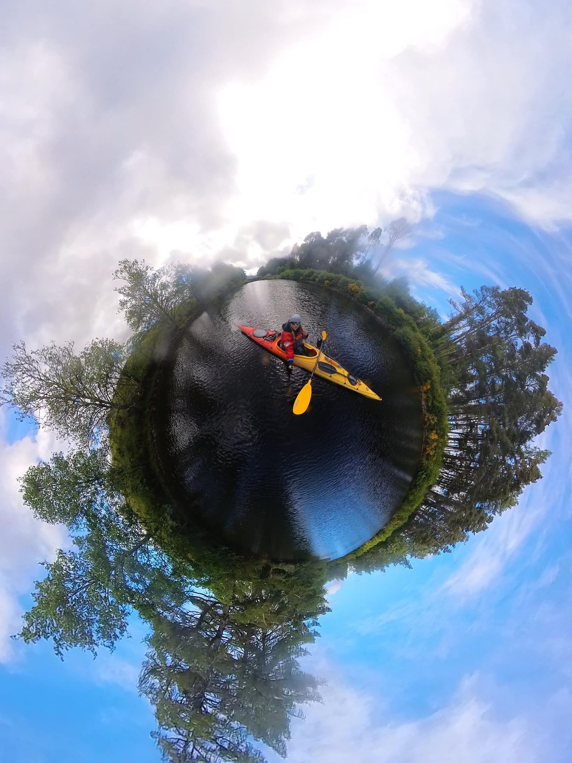 A person is paddling on the water in a canoe, surrounded by lush green trees and clear blue skies.