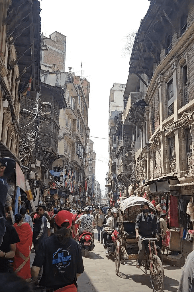 Kalabalık bir sokakta Nepal kültürünü yansıtan dükkanlar ve eski mimarilerle dolu bir manzara.