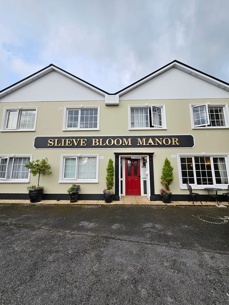 The front of the accommodation, Slieve Bloom Manor, is a building with a red entrance and a few potted plants next to it.