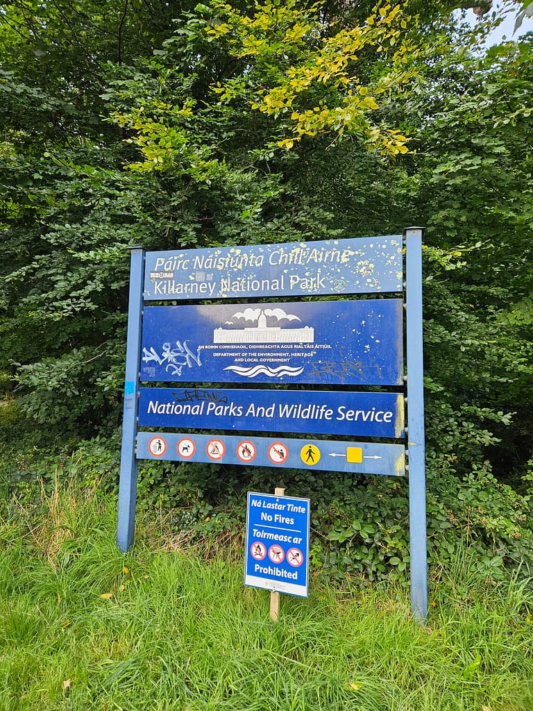 The sign indicating the entrance to Killarney National Park is surrounded by green vegetation.