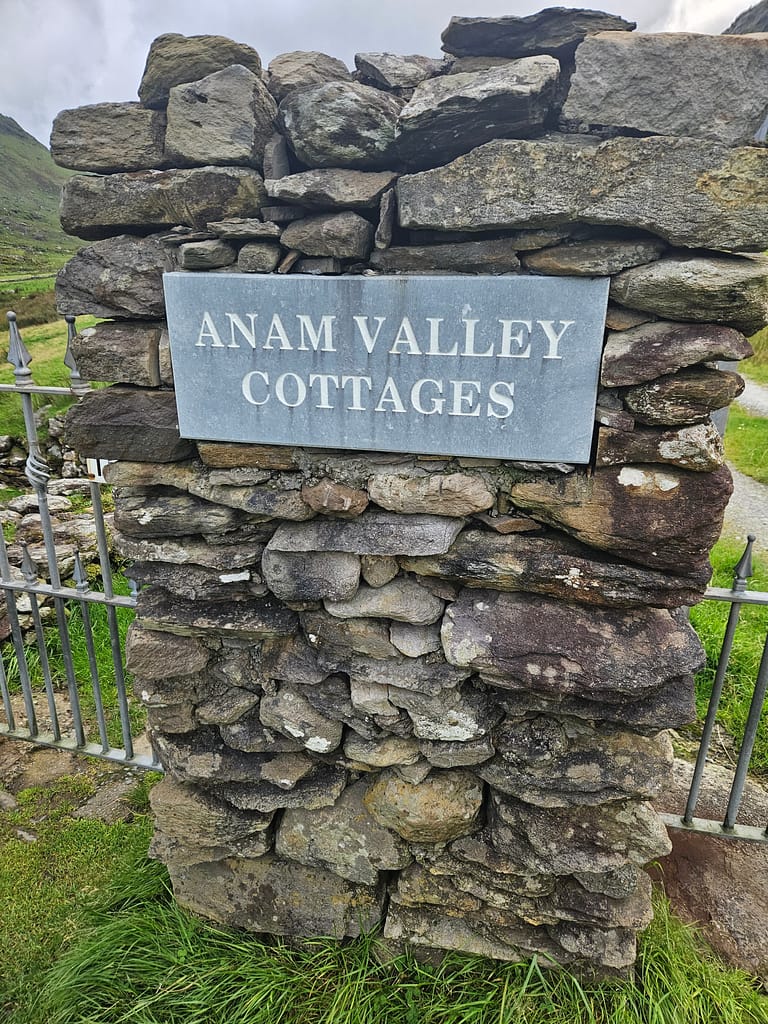 A natural stone wall with a sign that reads 'Anam Valley Cottages' attached to it.