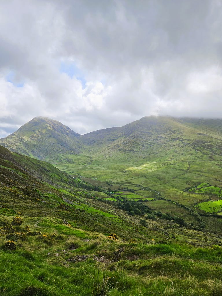 The wide landscape of green mountains and valleys, together with the slightly cloudy sky, offers a natural beauty.