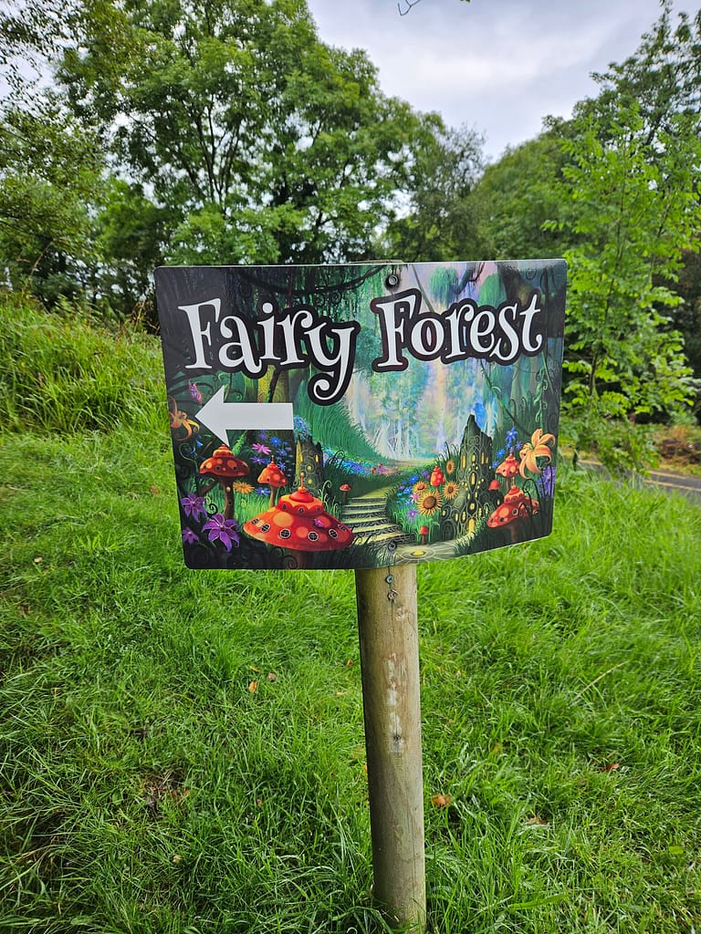 A colorful sign showing the direction to Fairy Forest is positioned among the green trees.