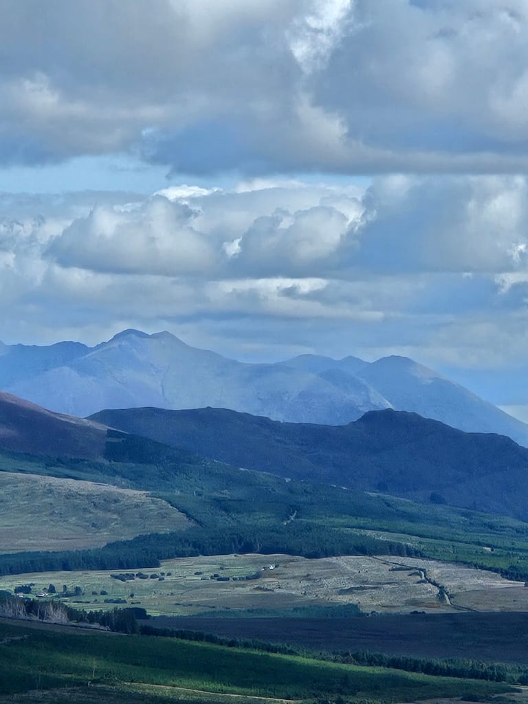 A mountainous landscape, vast lush green lands and cloudy skies.