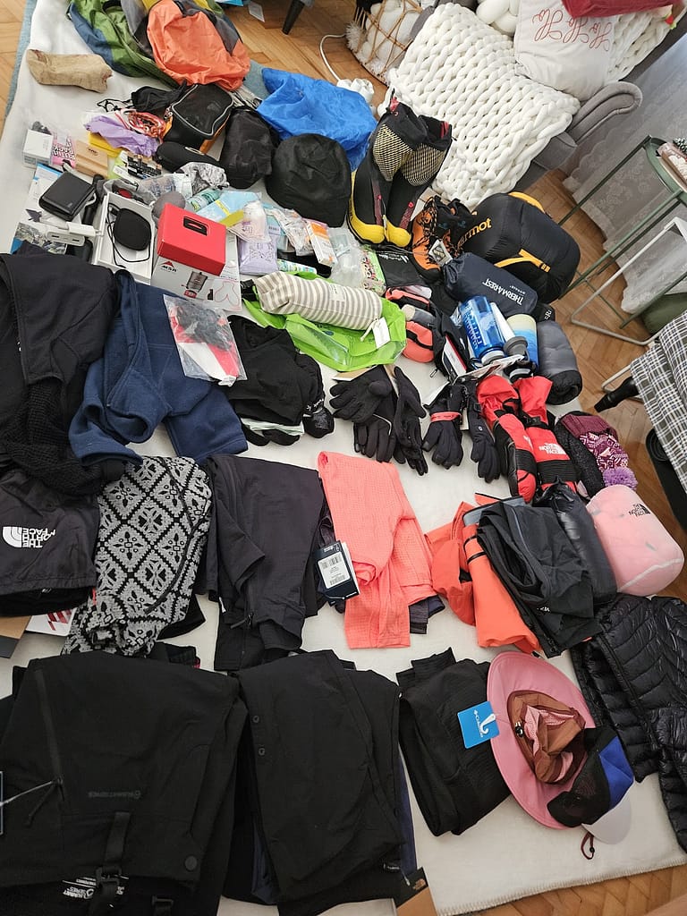 Everest Base Camp yürüyüşü için hazırlıklara dair dağcılık ekipmanları ve giysilerin yer aldığı bir masa görüntüsü.