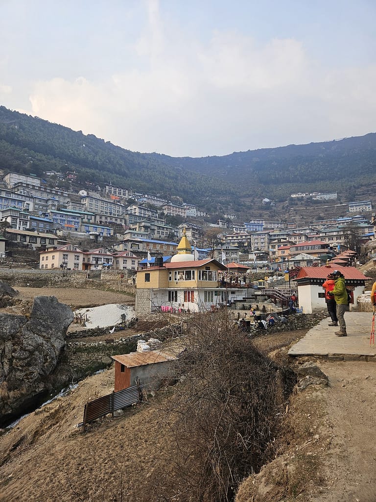 Namche Bazaar Himalaya köyünün manzarası, dağların eteğinde yer alan evler ve bir altın kubbeli yapı görünüyor.
