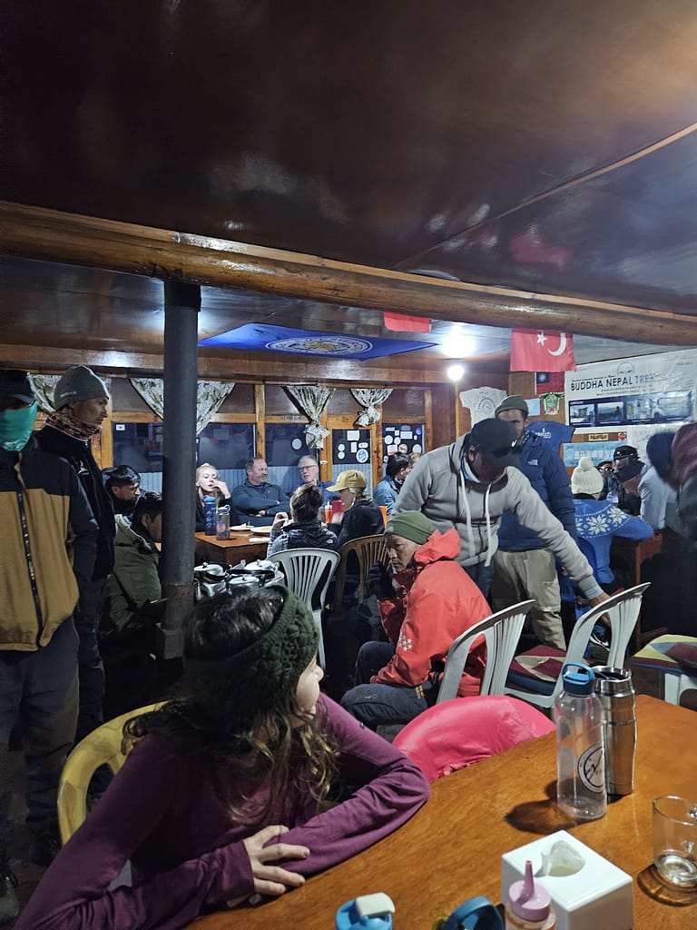 Kalabalık tea house'da oturan yürüyüşçüler, yemek masasında sohbet ediyorlar. Ortamda sıcak bir atmosfer hakim.