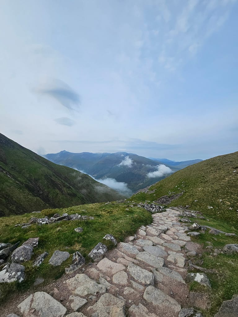 Un paesaggio che mostra pendii verdi e un sentiero di pietra su un sentiero escursionistico di montagna.