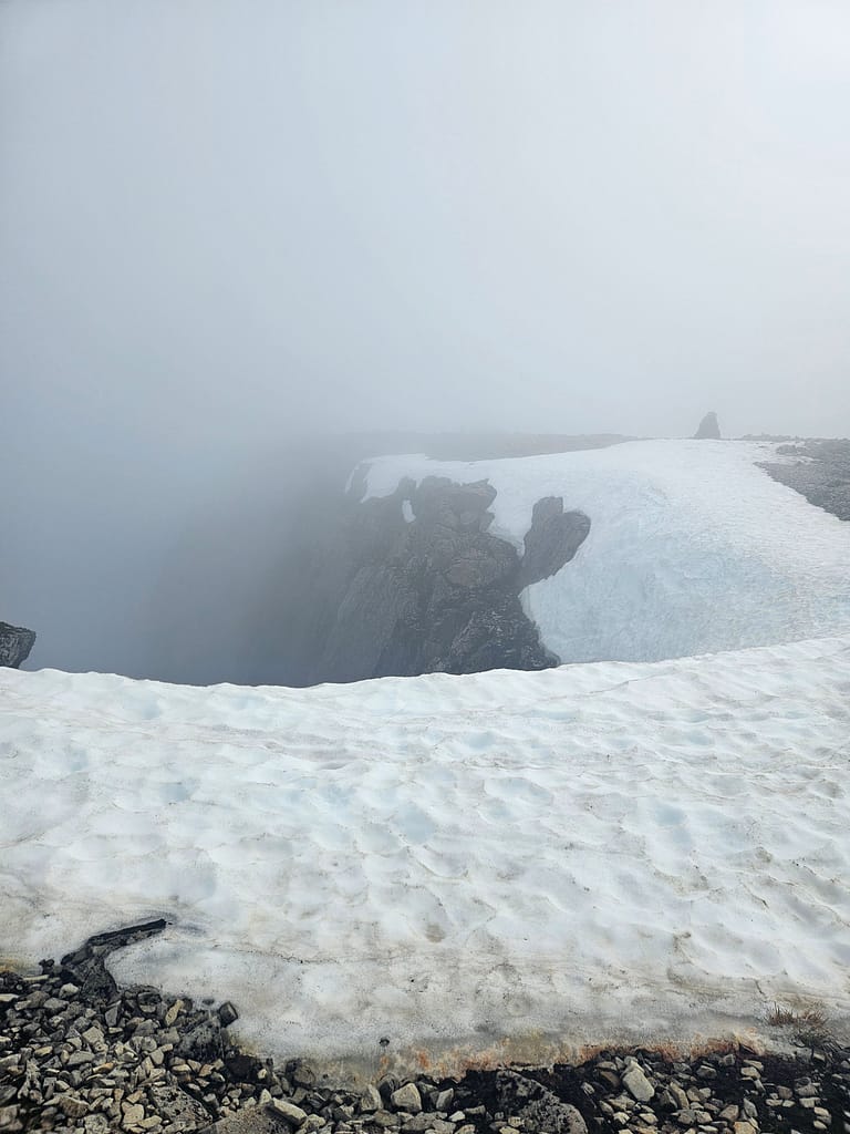 L'immagine è stata scattata dal bordo di una cima innevata in un clima nebbioso e mostra i dettagli delle rocce e della neve nella zona.