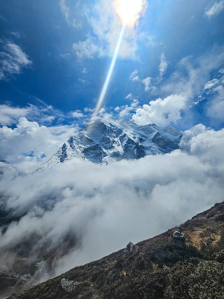 Buzul ve bulutların arasında parlayan dağ manzarası; güneşin ışınları dağın zirvesine vuruyor.