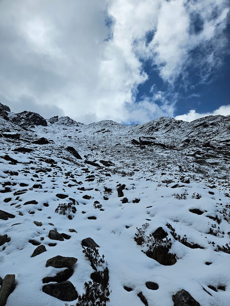 Karla kaplı dağlık bir alan, mavi gökyüzü ve beyaz bulutlarla birlikte yüce zirveler görünmekte.