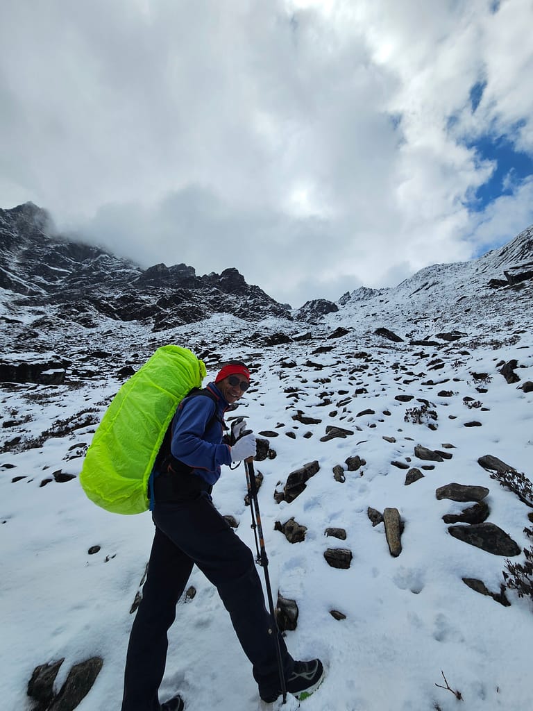 Bir dağcı, karla kaplı arazide yürürken, üzerinde büyük bir neon yeşili sırt çantası ve dağcı ekipmanlarıyla poz veriyor.