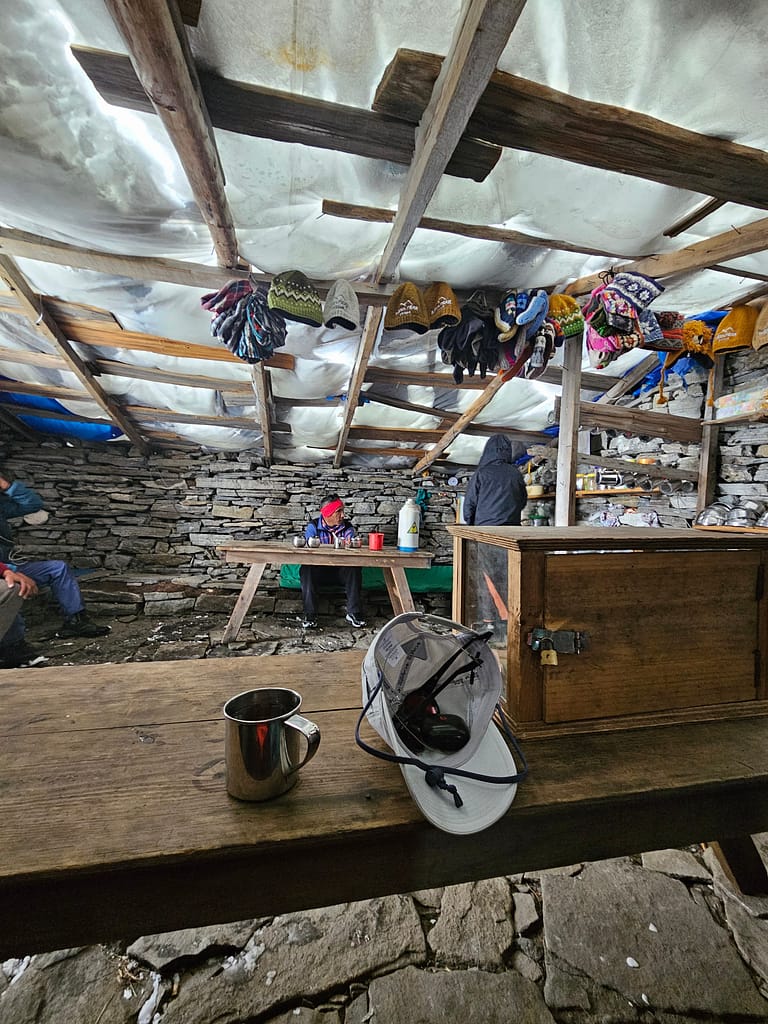 Bir dağ evinin içi, ahşap masalar, metal bir kupa ve şapka ve eldivenlerin raflarda asılı olduğu bir manzara.