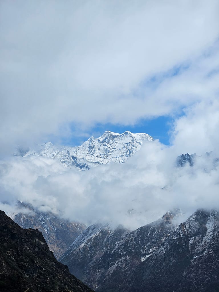 Himalaya dağlarının üst kısmında, gökyüzünün mavi ve beyaz bulutlarla dolu bir görüntüsü, karla kaplı zirvelerin aralarında belirdiği bir manzara.