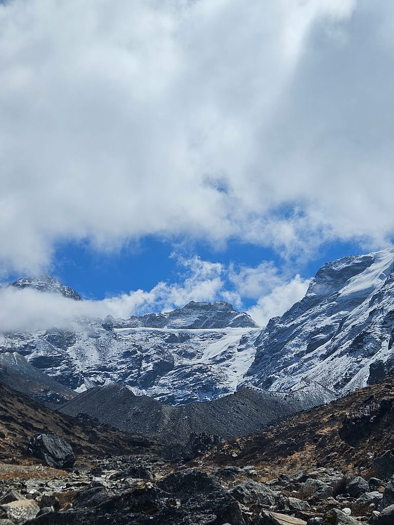 Karlarla kaplı yüksek dağlar ve mavi gökyüzü arasında bulutlar görünmektedir.