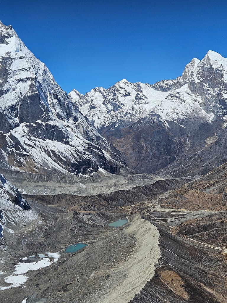 Buzul ve taşlarla dolu dağ vadisi manzarası, yüksek zirveler arka planda görünmektedir.