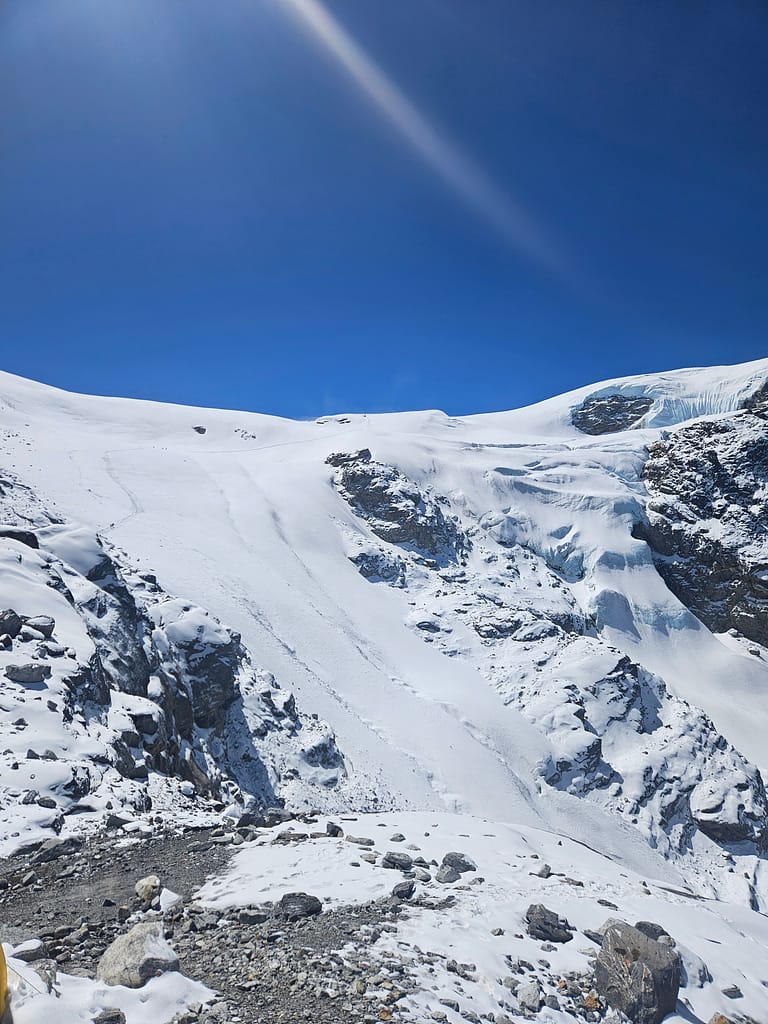 Buzul ve kayalarla kaplı dağ manzarası, açık mavi gökyüzü altında.