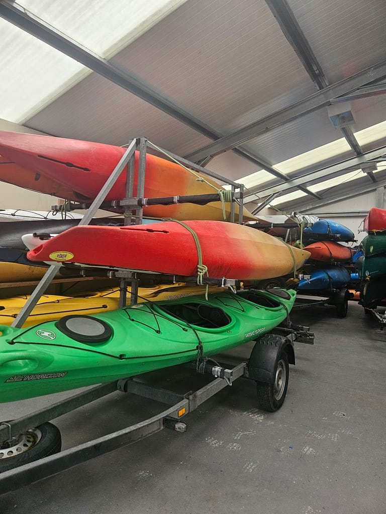 An area where canoes and kayaks are stored, with canoes and kayaks of different colors stacked on top of each other.