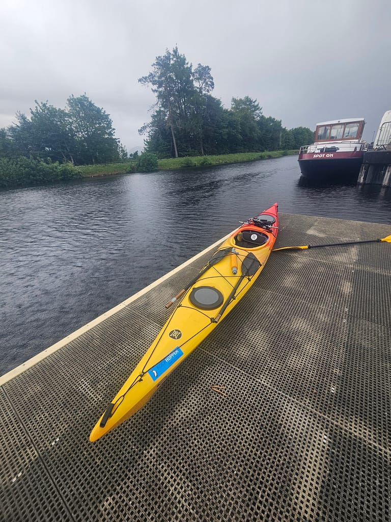 A boat and surrounding trees are visible on the water in a harbor. The sky is cloudy and the weather is overcast.