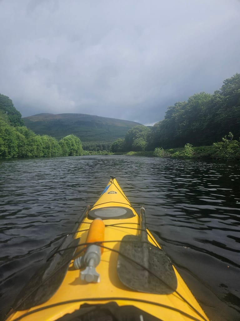 A view from the perspective of a person canoeing across a lake, a waterway surrounded by forest and mountains.