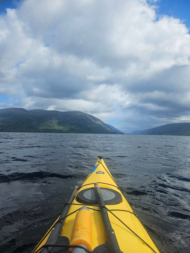 Mountain views and cloudy skies appear as a canoe moves across the peaceful water.
