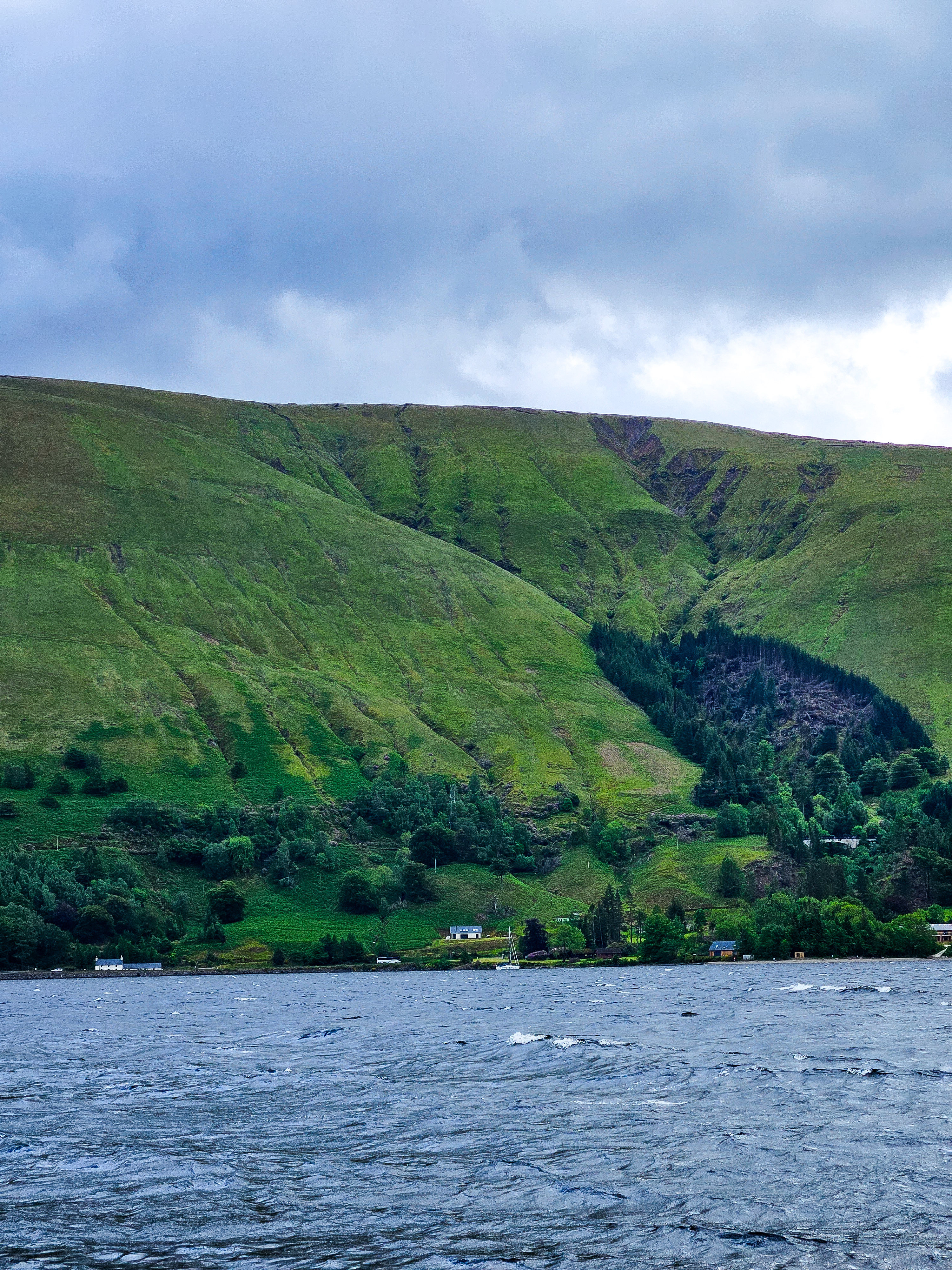 A lake and surrounding lush mountains are captured under a cloudy sky.