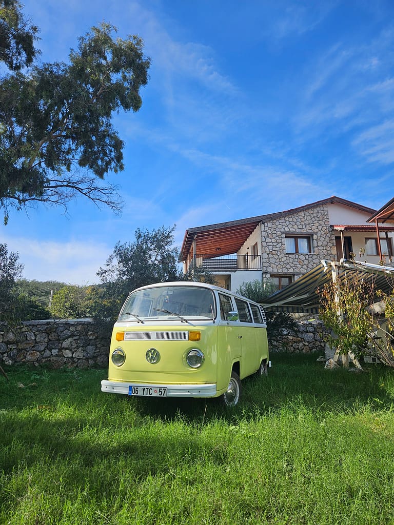 A vintage yellow Volkswagen van parked on green grass in front of a stone house under a blue sky.