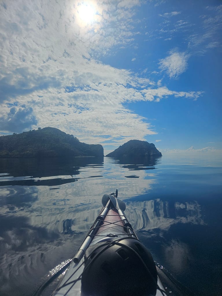 Deniz kayığı ile sakin bir su üzerinde, gökyüzünde bulutlar ve güneş yansırken görünüm.