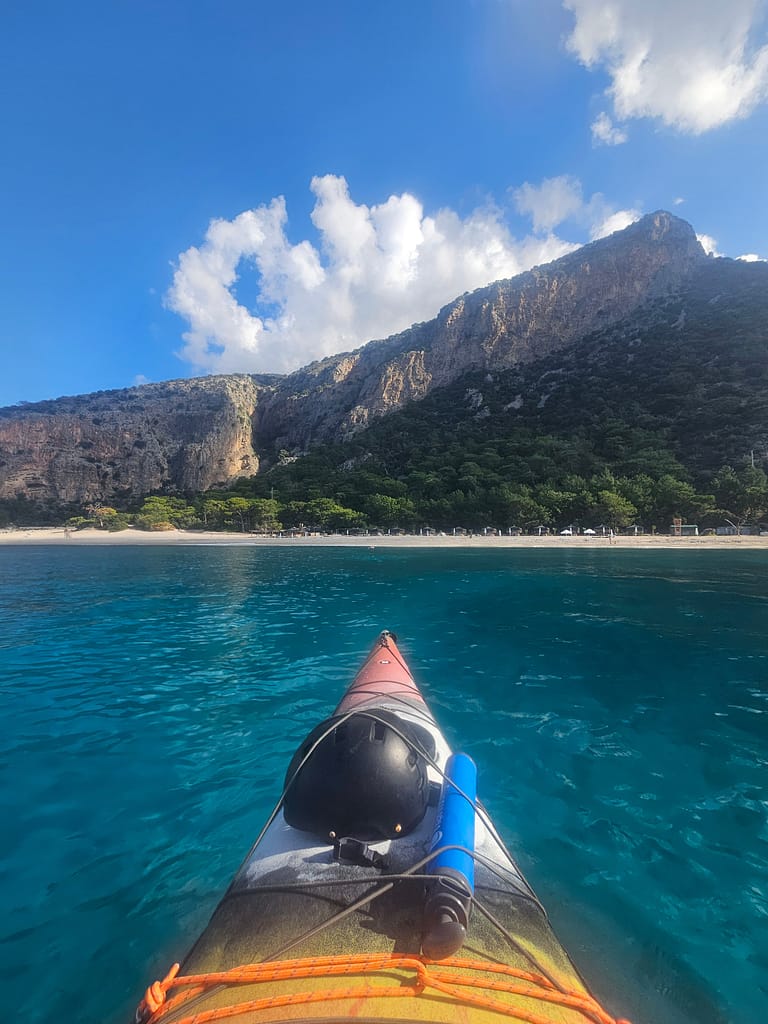 Deniz kayığı ile mavi sularda ilerleyen bir manzara, arka planda yemyeşil ağaçlar ve yüksek kayalıklarla çevrili.