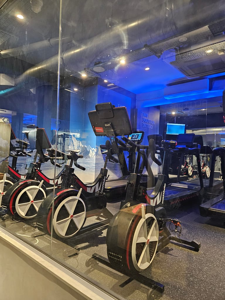 Bir spor salonunda yüksek irtifa simülatörlerinin bulunduğu alan, egzersiz ekipmanları ve mavi ışıklandırma ile dekoratif bir görünüme sahip.