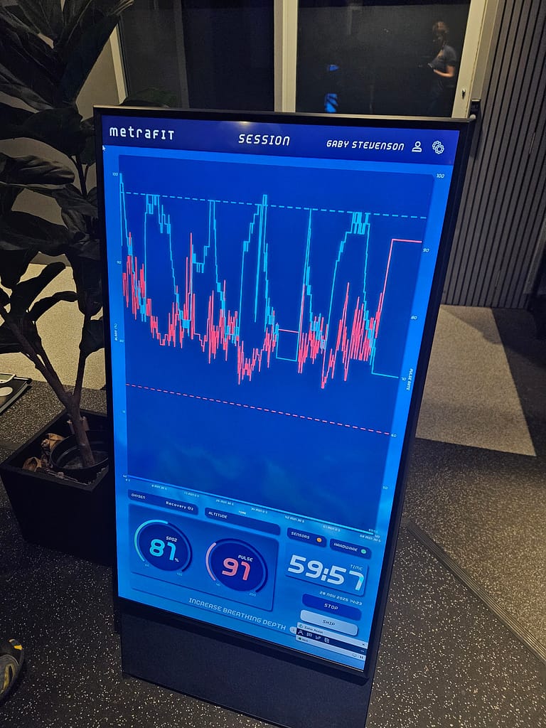 Bir ekran üzerinde oksijen saturasyonu, nabız ve irtifa değerlerini gösteren grafik ile ölçüm cihazı. Ekran, dağcılık ve yüksek irtifa eğitiminde kullanılan bir simülatör alanında yer alıyor.