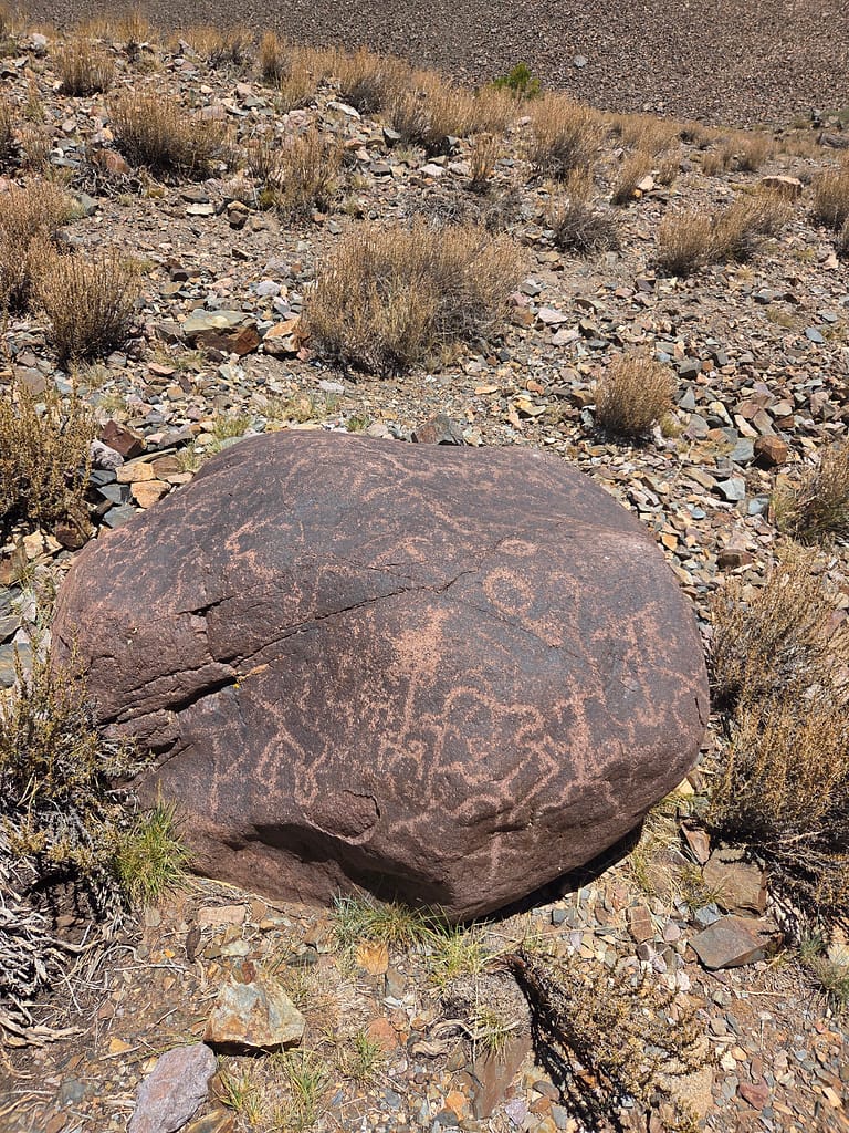 Sahada duran büyük bir taş üzerinde eski insan yapımı çizimlerin bulunduğu bir görüntü.