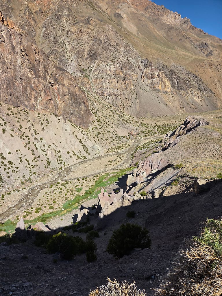 Yüksek dağlık bölgede, derin bir vadide uzanan kayalık alanlar ve yeşil çayırlıklar.