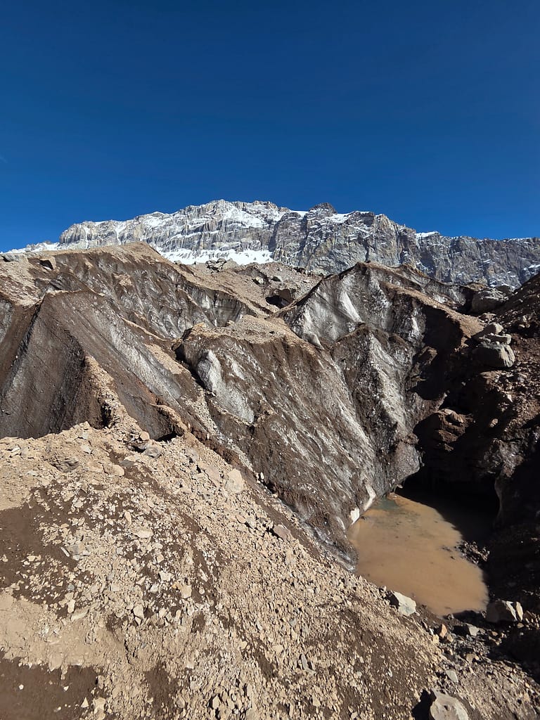 Karlı dağların arka planda yer aldığı, taşlık bir arazideki doğal manzara.