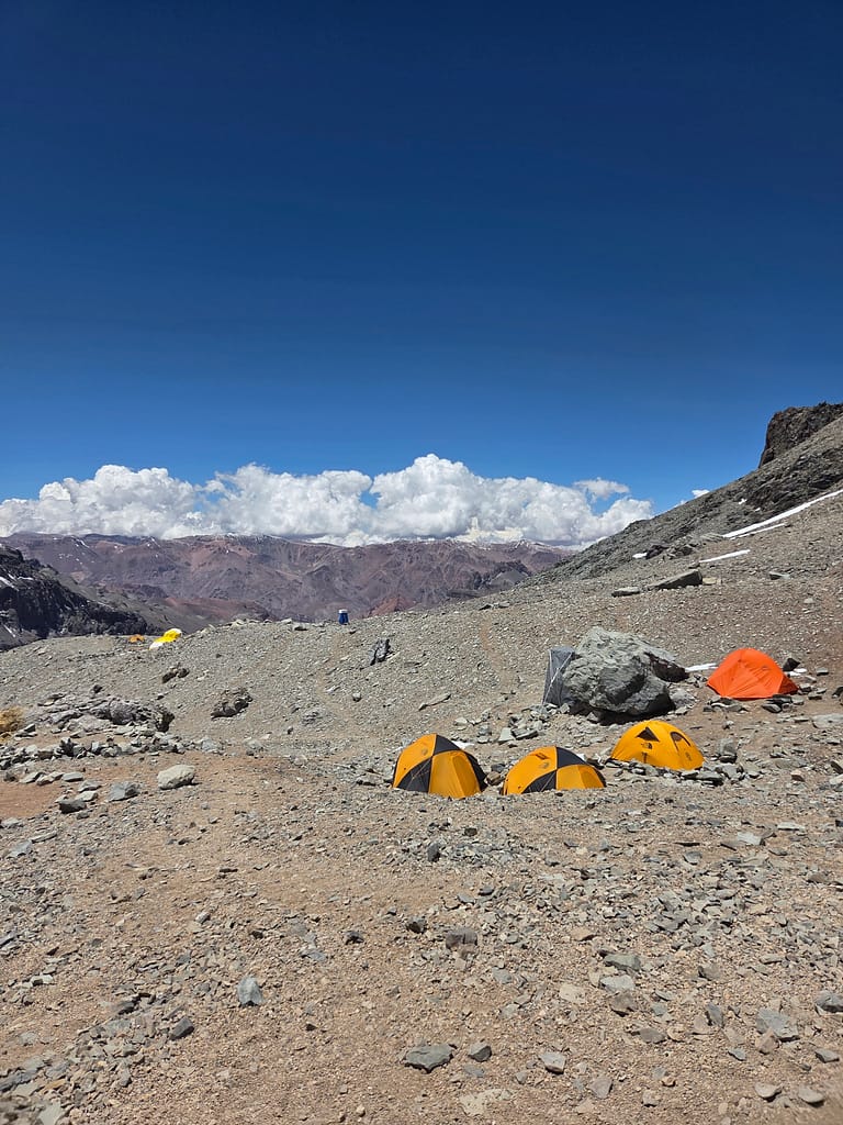 Dağlık bir alanda dizilmiş turuncu çadırlar ve mavi gökyüzü arka planda.