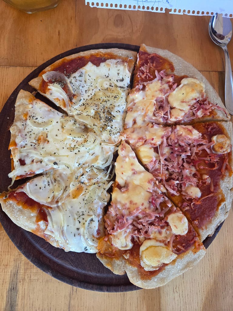 Dört dilimden oluşan yarım pizza, bir yarısı beyaz sos ve soğan, diğer yarısı domates sos, jambon ve peynir ile süslenmiş.