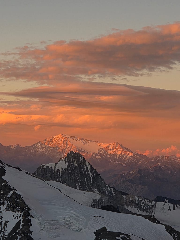 Güneşin batışı sırasında aydınlatılan karla kaplı dağların ve bulutların manzarası.
