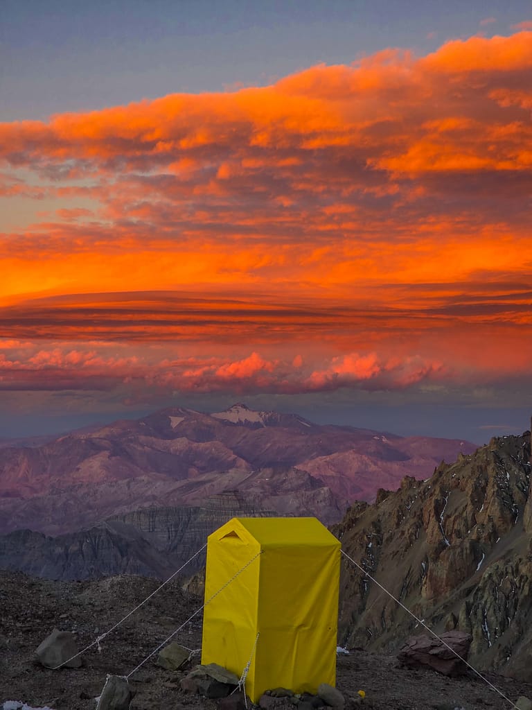 Renkli bir gün batımının önünde dağ manzarası ile sarı bir tente.
