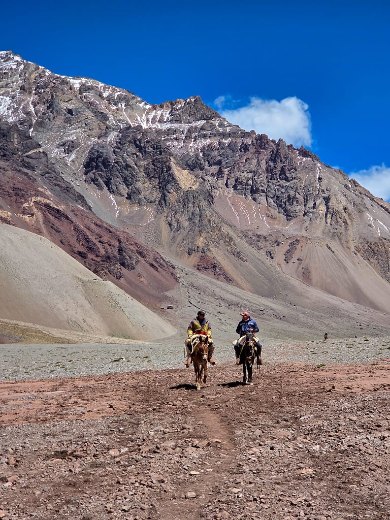 Dağlık bir alanda iki kişinin at üzerinde yürüdüğü bir manzara.